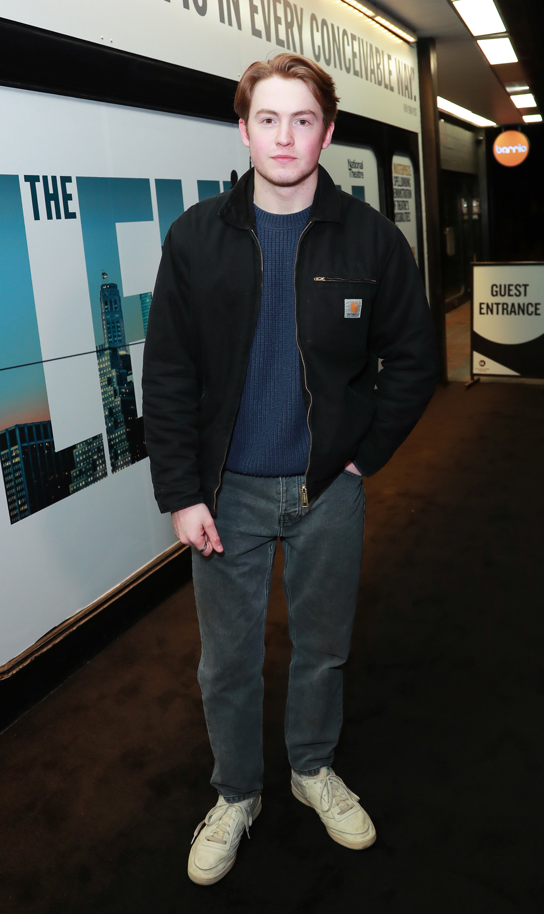 Kit is wearing jeans, a sweater, zip-up jacket, and sneakers