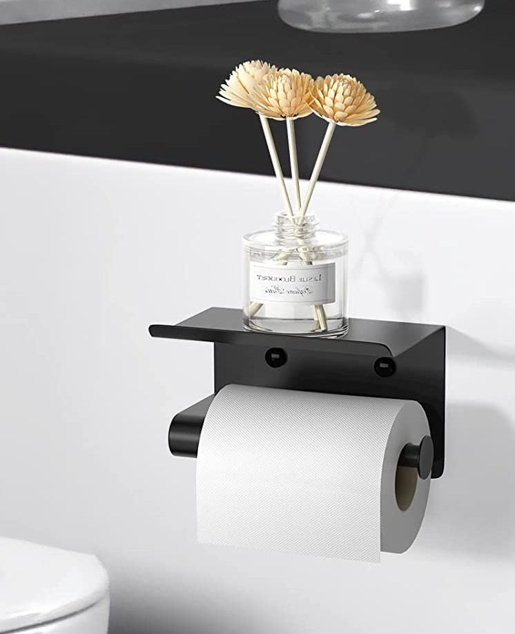 the toilet paper holder with a vase of flowers on the little shelf