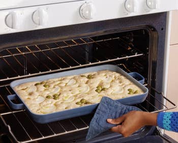 A hand pulling out the blue pan from the oven
