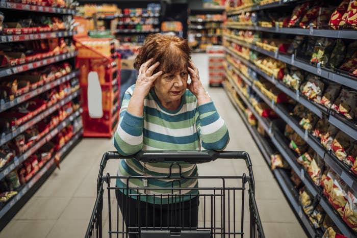 A woman holding her head in her hands as she stands in a grocery store aisle