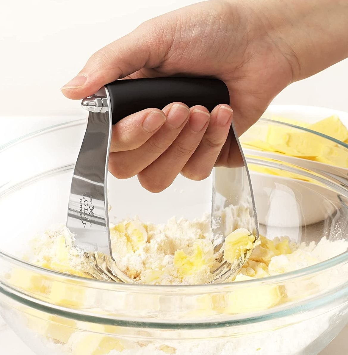 A person mixing butter and flour in a bowl with the dough cutter