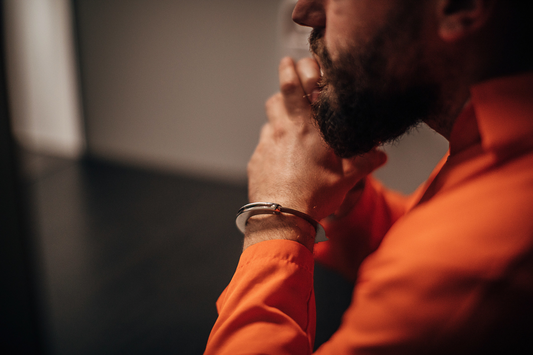 A man in an orange jumpsuit with hands handcuffed