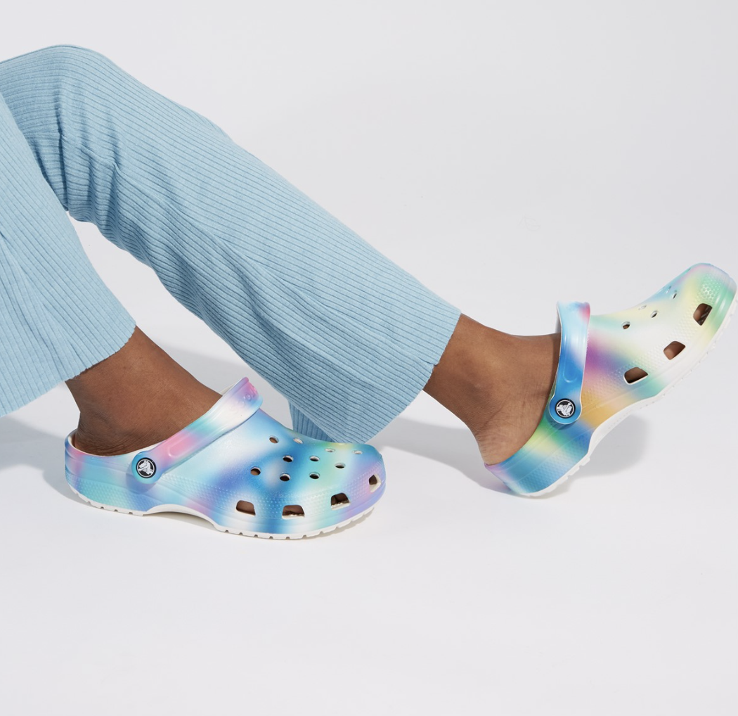 a model wearing a pair of multi coloured crocs against a plain background