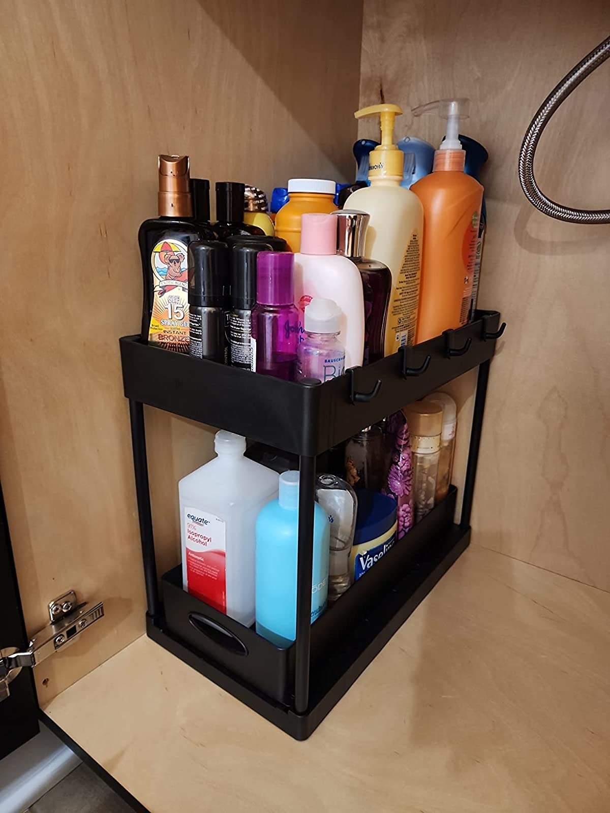 A black storage organizer filled with various personal care products in a wooden cabinet