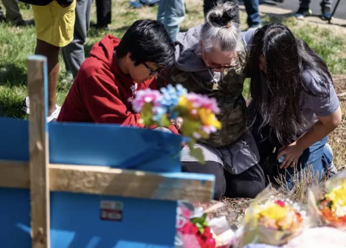 three people kneel on the ground in front of a vigil site with flowers after the nashville school shooting