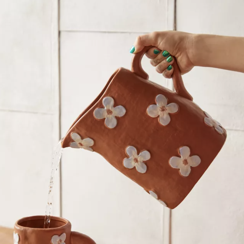 someone pouring water out of the chunky pitcher that has a daisy design