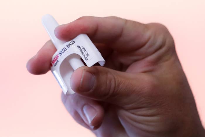 A hand holds up a small plastic device labeled "Narcan Nasal Spray"