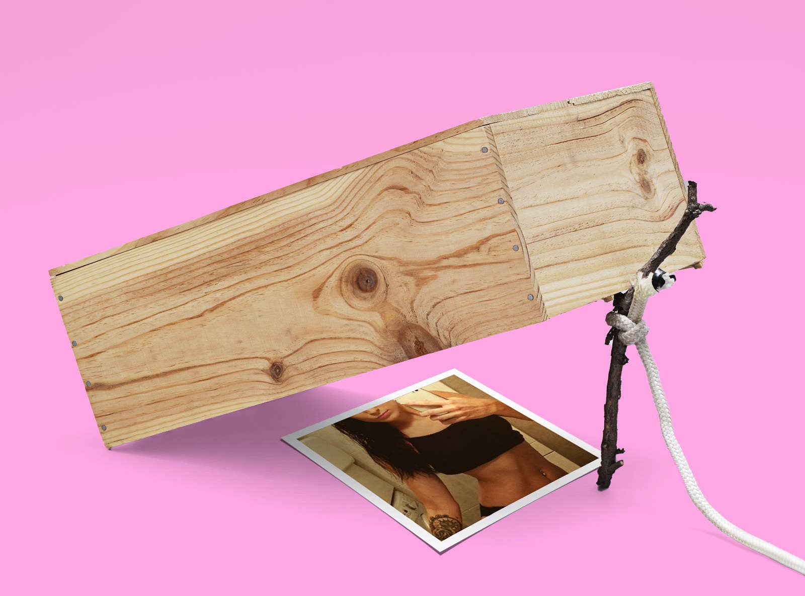 A rudimentary trap shows a wooden box propped up by a stick attached to a rope on top of a seductive mirror selfie showing a woman wearing a black top