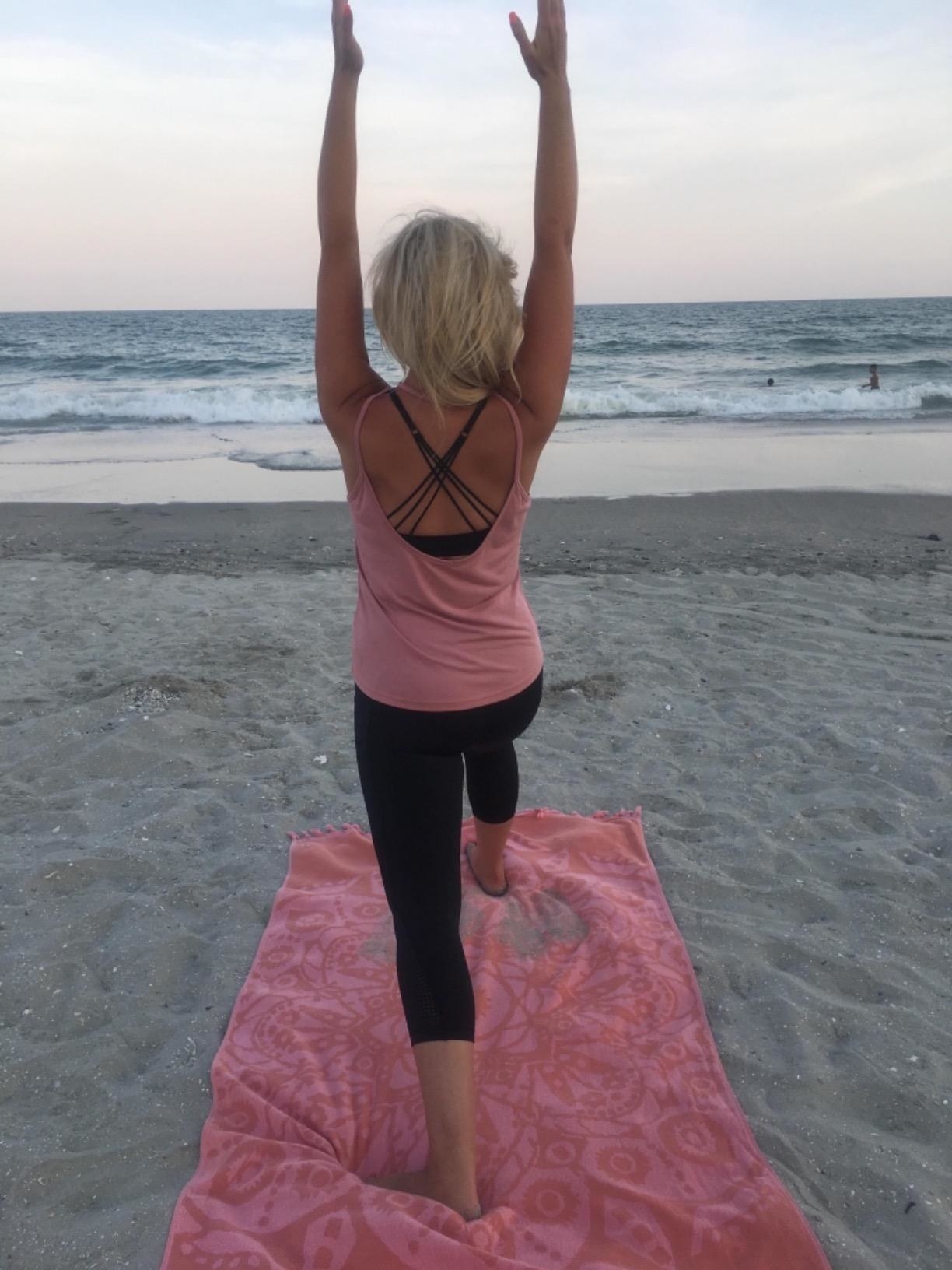 Reviewer wearing black leggings while doing yoga on the beach