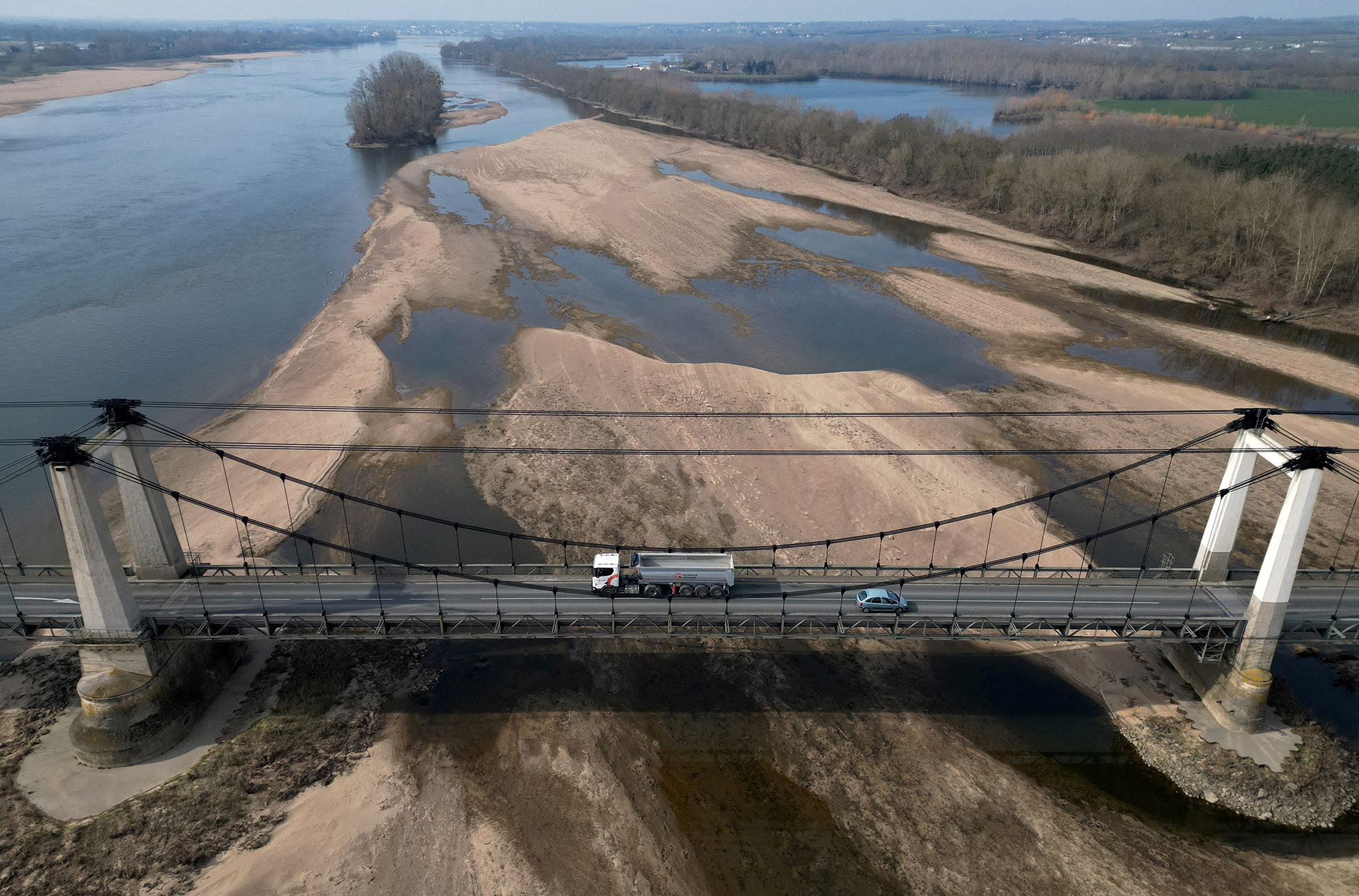 aerial shot of a truck driving over a bridge, below the bridge is dry. land and patches of water