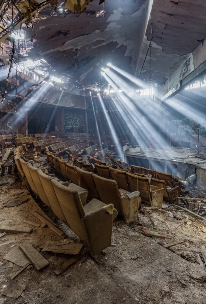 The floor and seats of the theater are falling apart, while large holes in the ceiling cause the room to be bathed in light