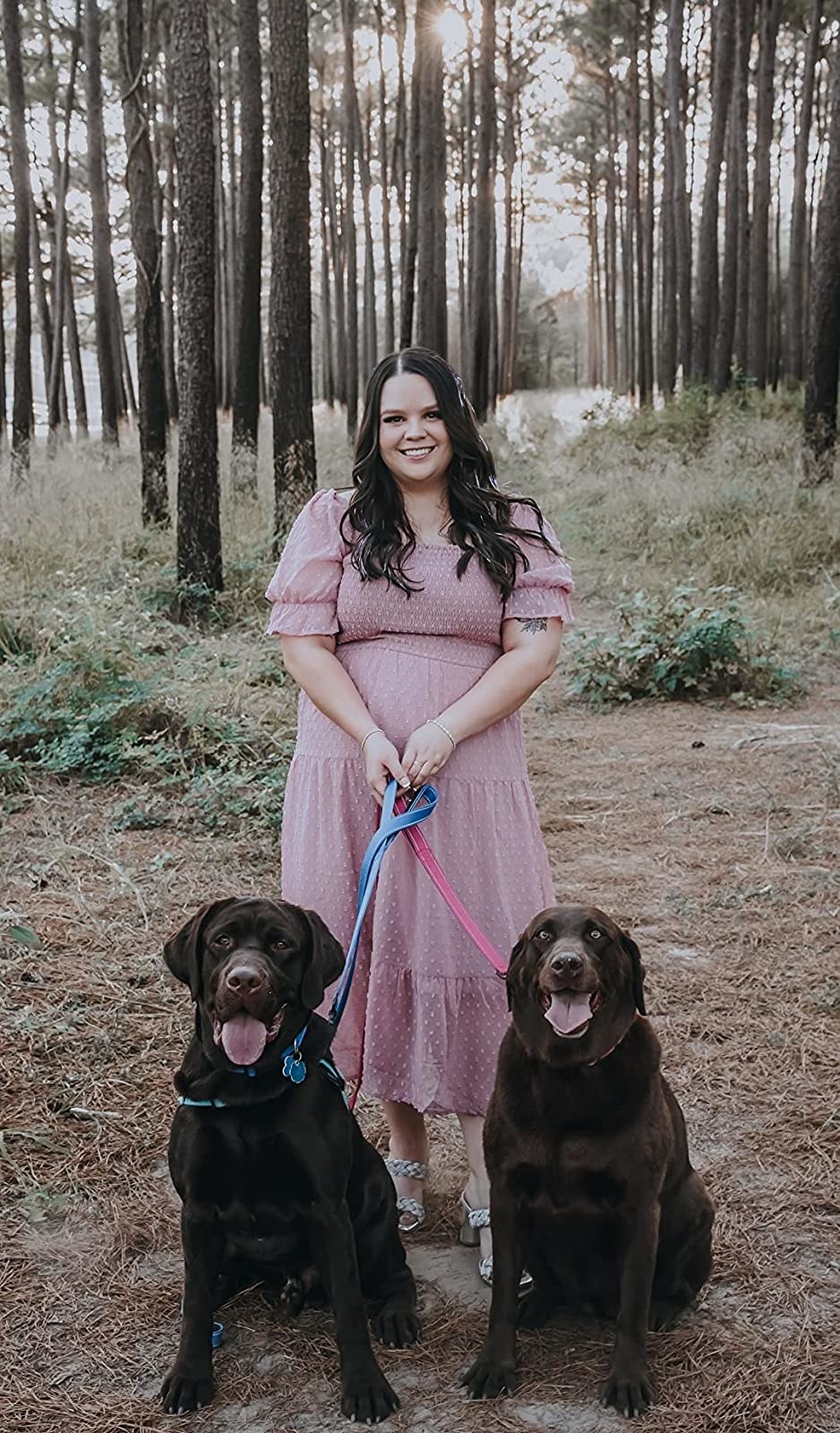 A reviewer wearing a pink dress with two chocolate labs