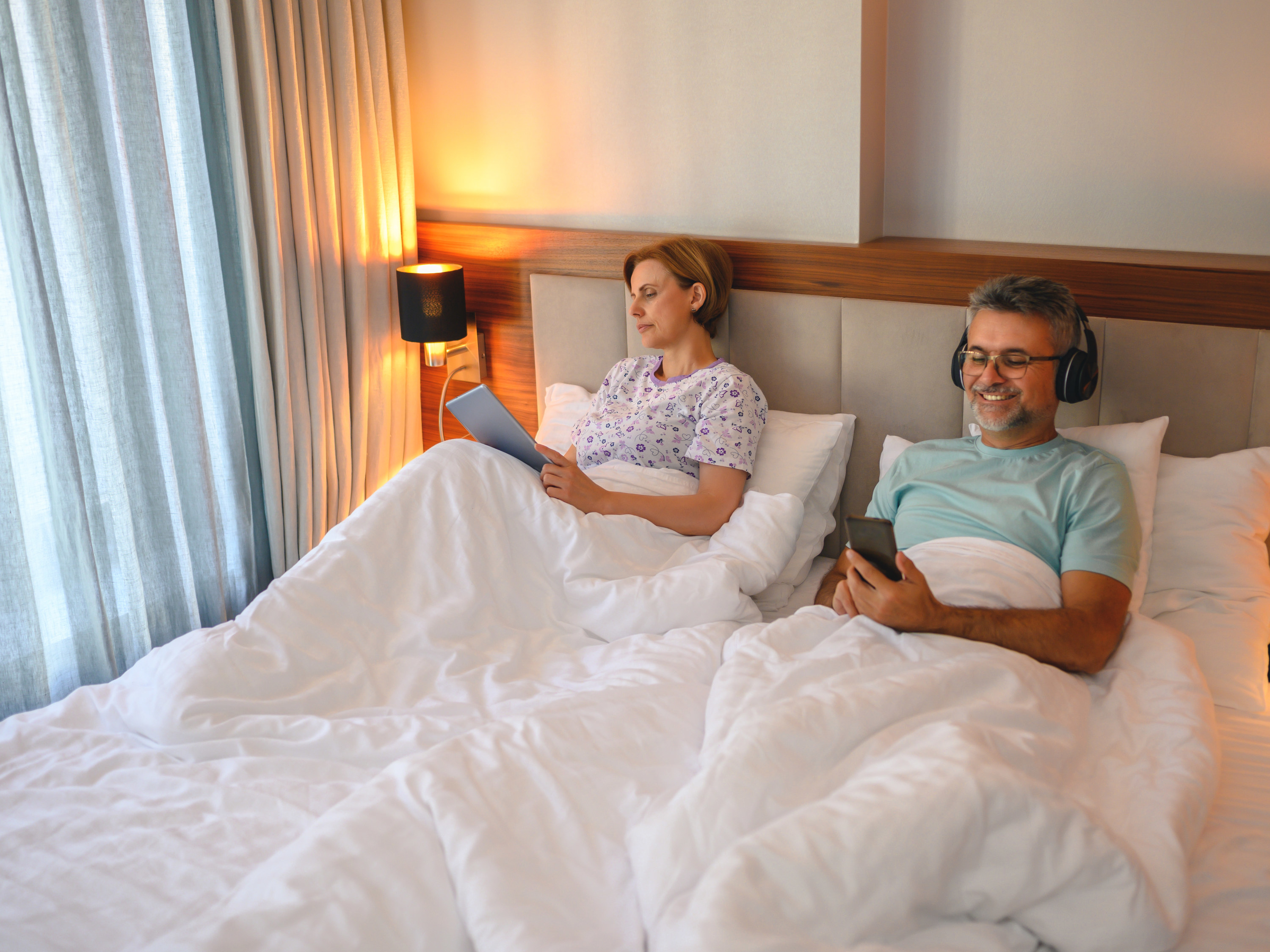 Couple lying in bed using mobile phone and tablet while ignoring each other