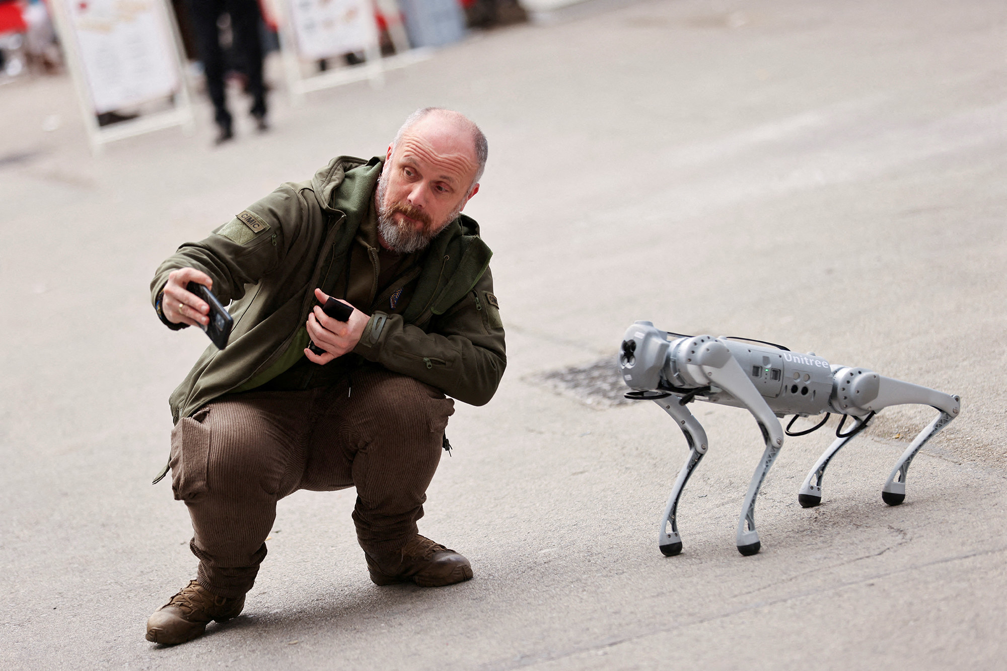 A kneeling man takes a selfie with a cellphone next to a four-legged robotic dog