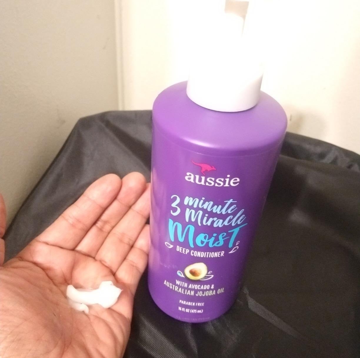 a hand next to the bottle holding a bit of the conditioner