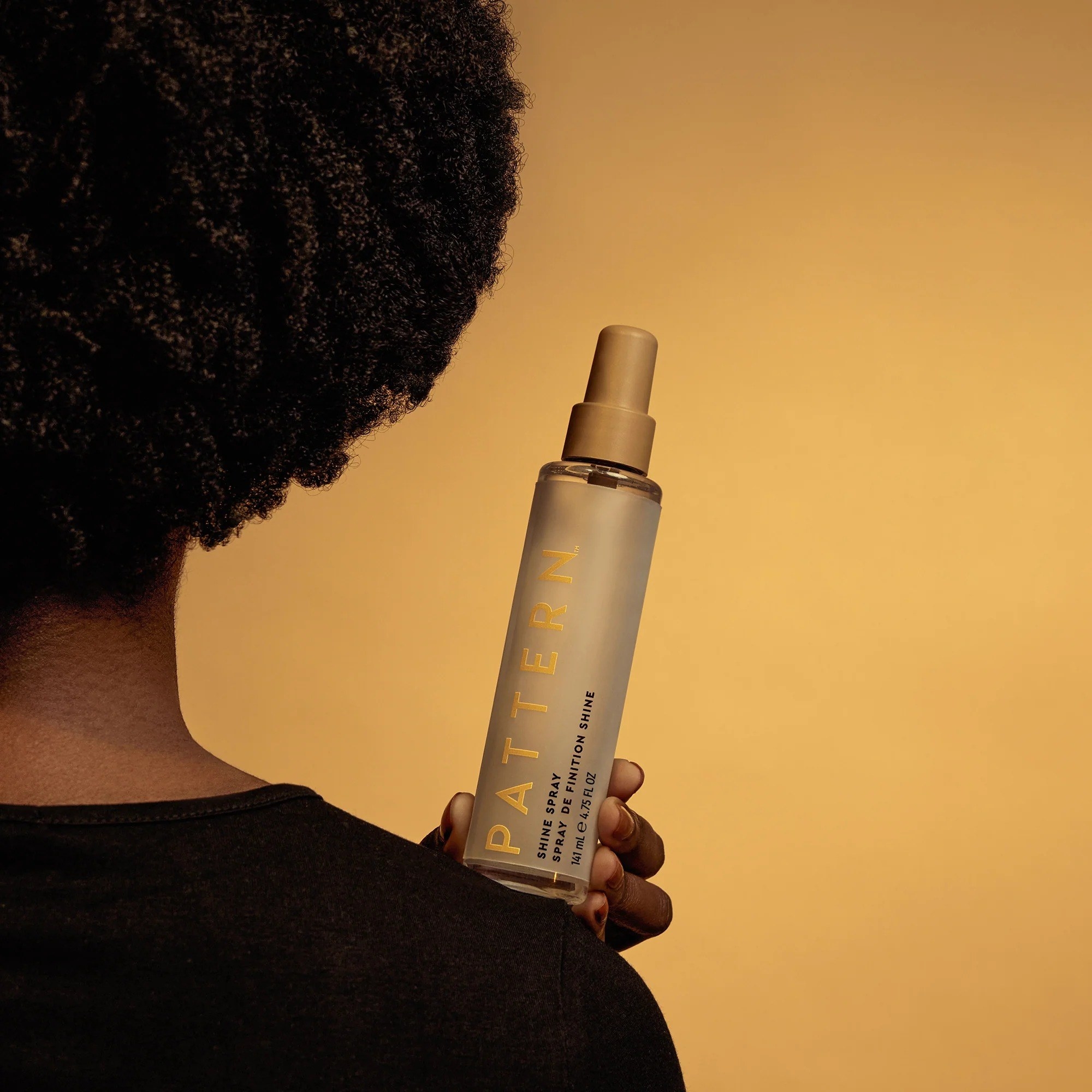 a model holding the shine spray over their shoulder