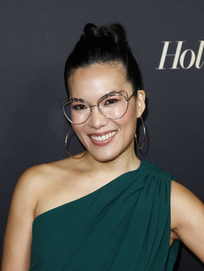 Ali Wong smiles for a photo at an event. She&#x27;s wearing a one-shouldered outfit that ruched at the top of the shoulder and large hoop earrings. Her hair is swept into an updo