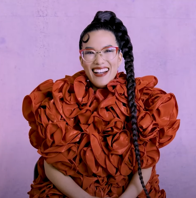 Ali Wong laughs during an interview with the Hollywood Reporter. She&#x27;s wearing a voluminous ruffled dress and her hair is styled into an ultra long single braid