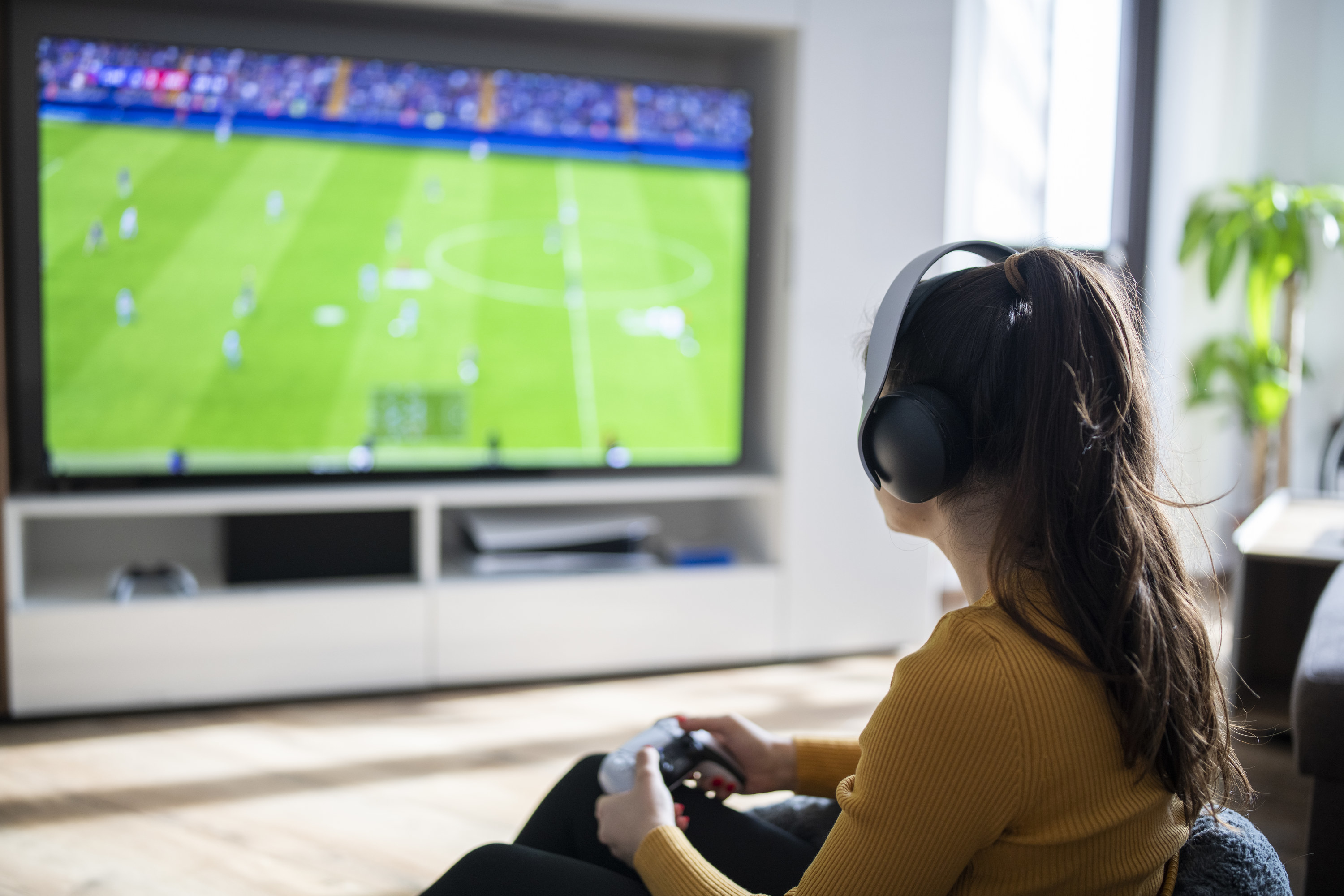 Rear view of woman playing football game on a gaming console at home
