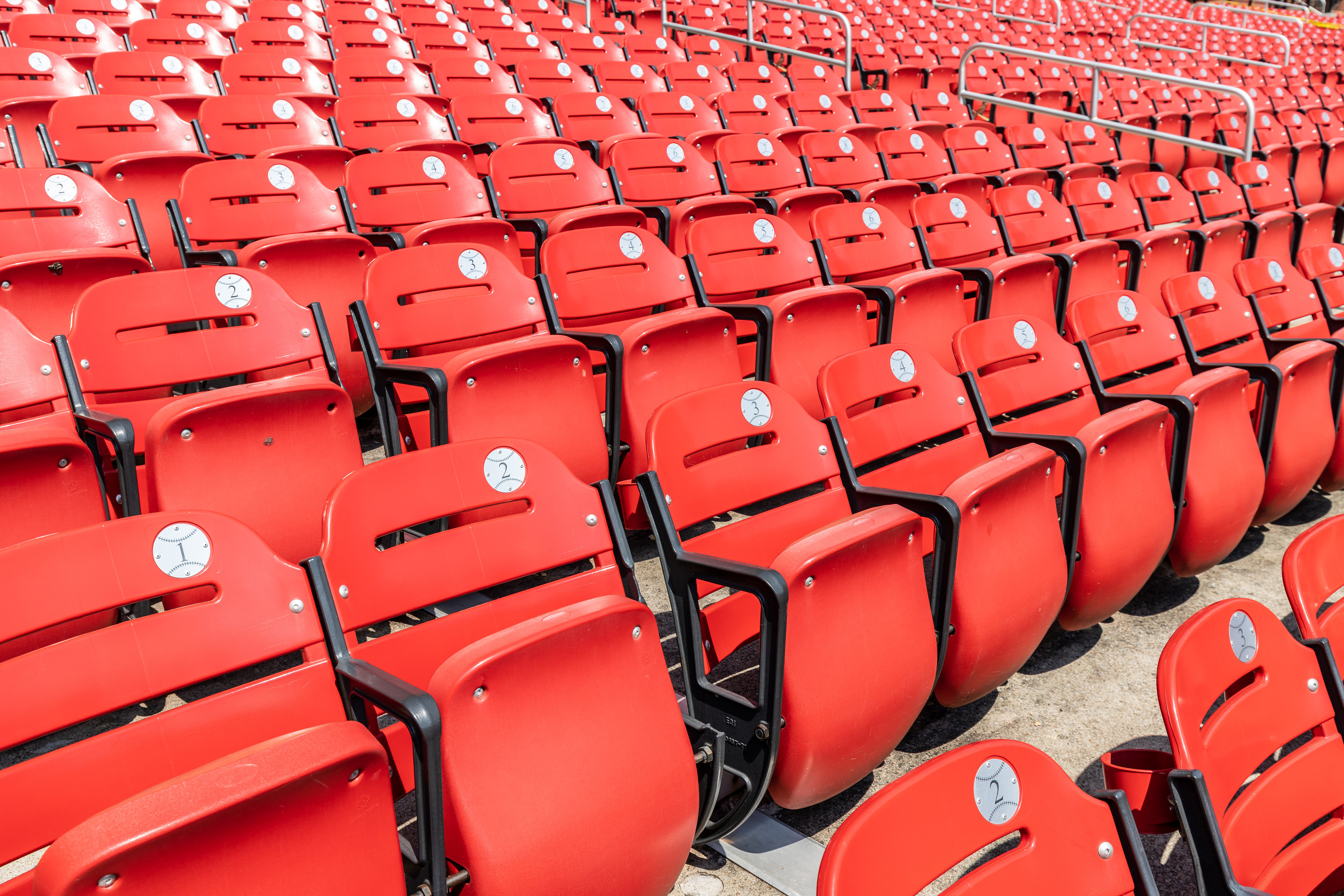 Rows of empty red bleacher seats in a stadium with numbers inside of baseball looking stickers