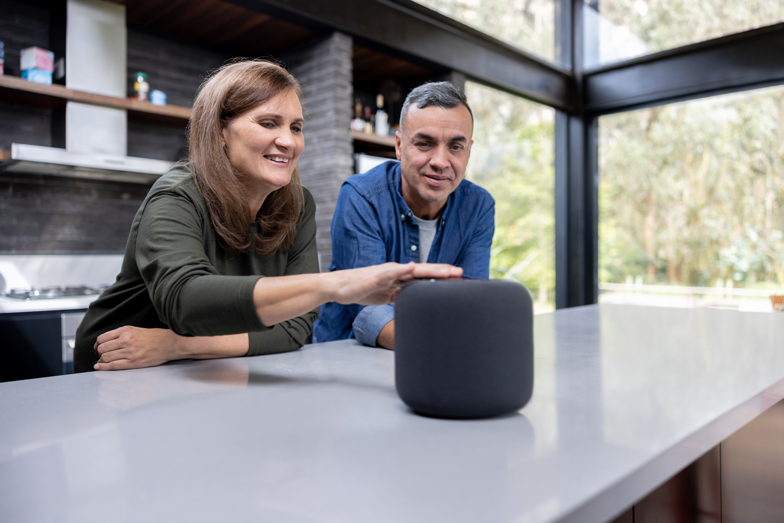 Happy Latin American couple at home using a smart speaker