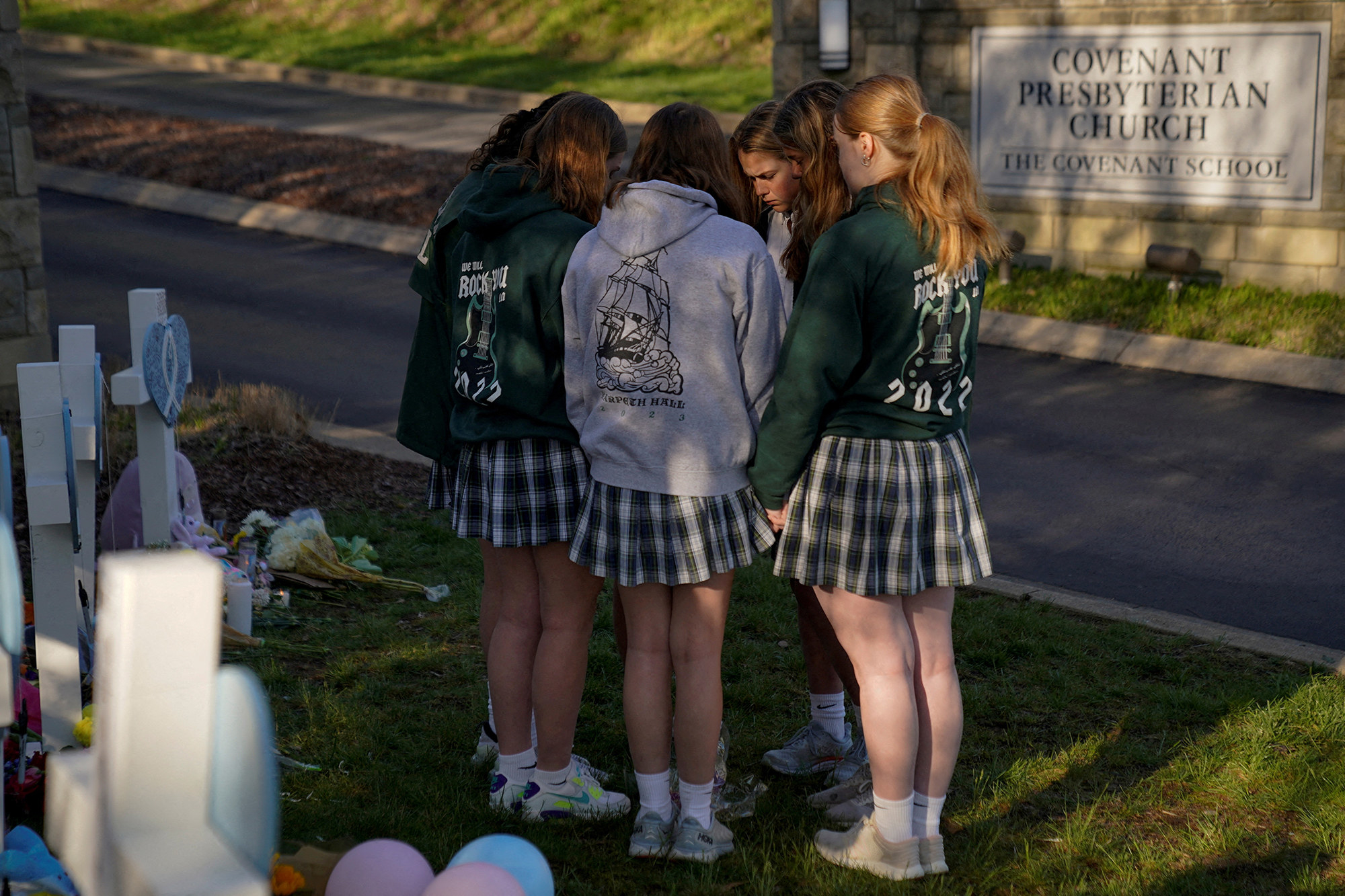 a small group of students huddle in prayer next to a memorial