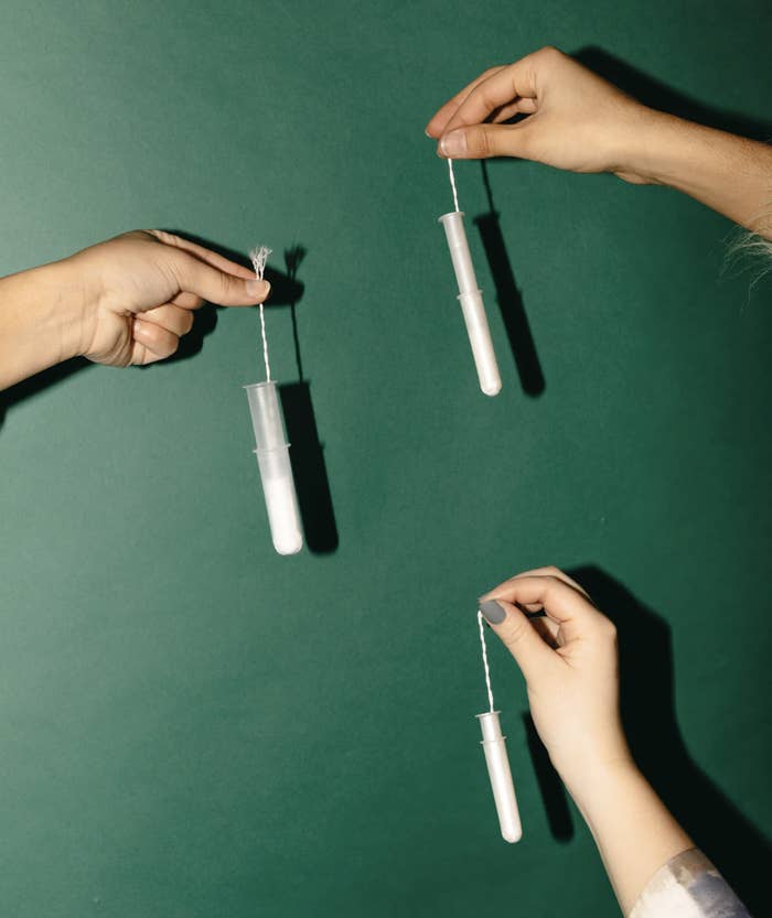 a trio of hands each holding a tampon by the string