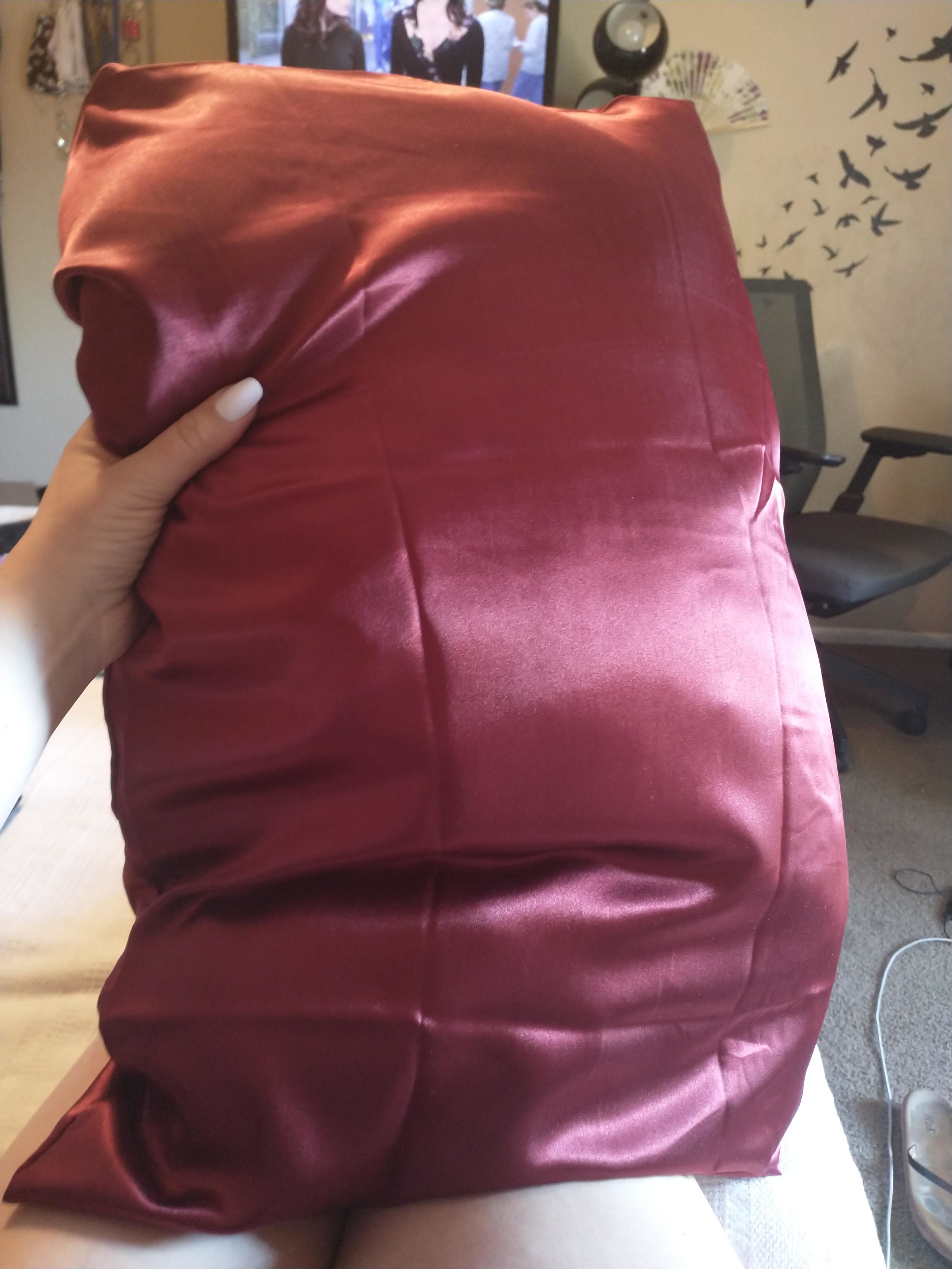 Reviewer holding up pillow with the burgundy satin pillowcase on it