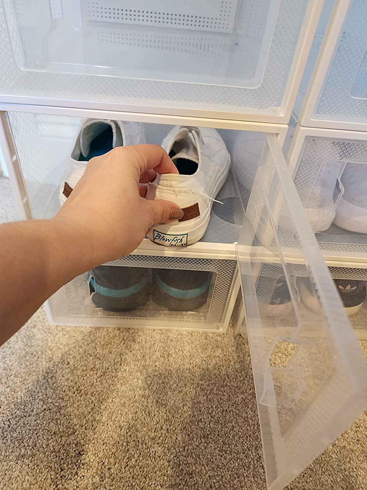 a reviewer photo showing a hand putting a pair of white sneakers in one of the clear boxes in a stack