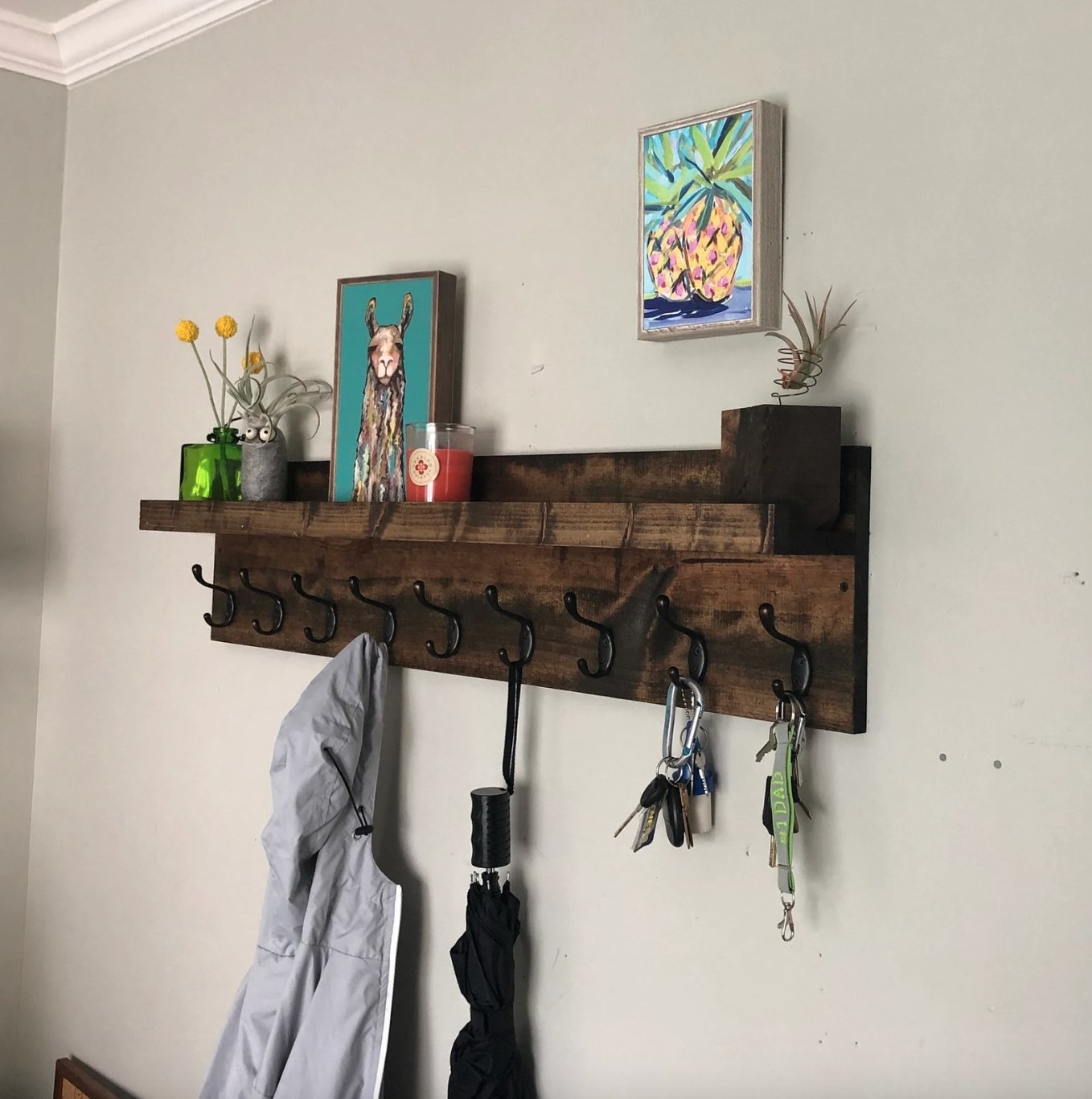 the distressed wood coat rack with shelf hanging on a wall, and with a coat, umbrella, and keys hanging from the hooks