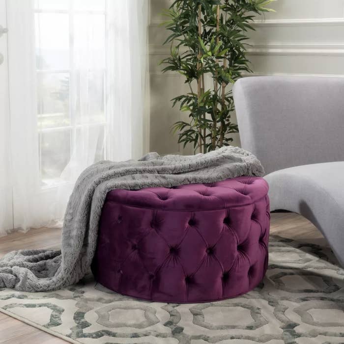 The plum ottoman with blanket draped on it