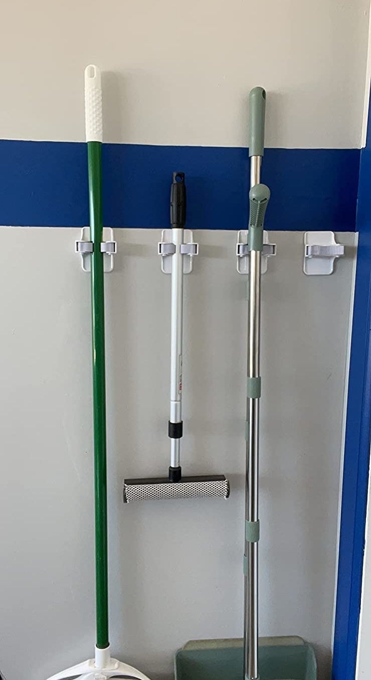 a reviewer photo of the grippers holding a broom, squeegee, and dustpan on a blue and white wall