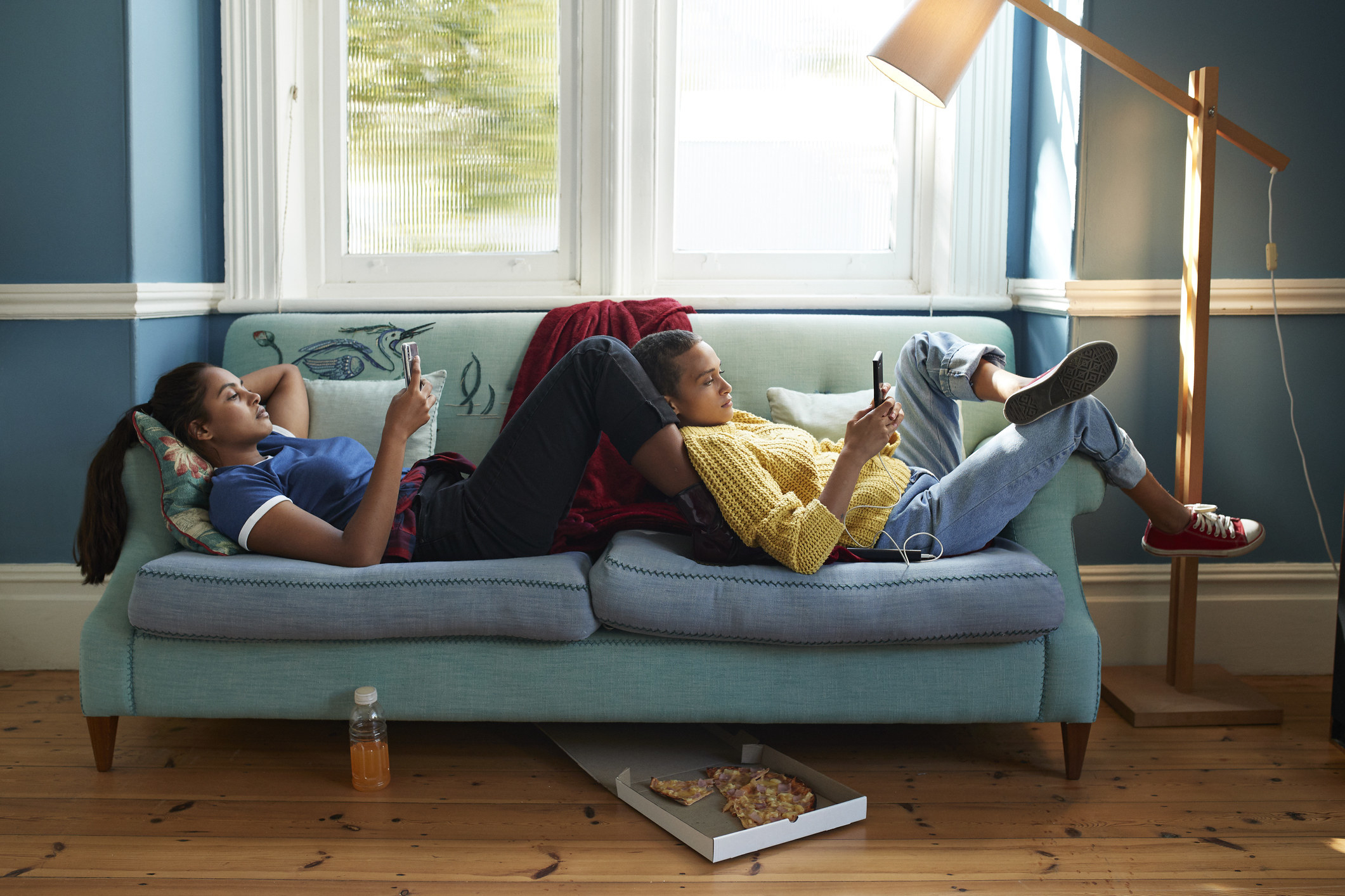 Two women laying on a couch on their cellphones