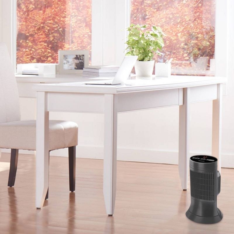 A sleek, compact air purifier placed on the floor beside a minimalist white desk with decorative plants