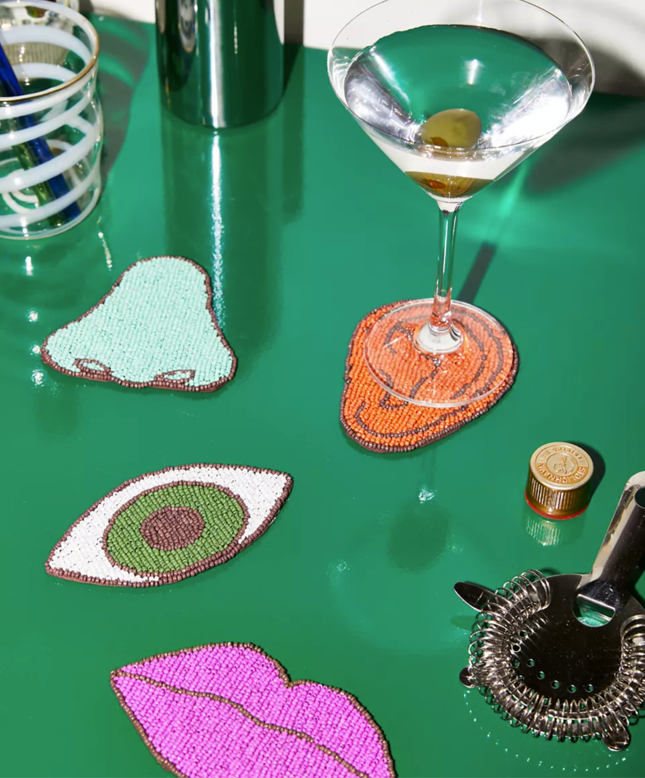 The four beaded coasters on a table, one with a martini glass on it