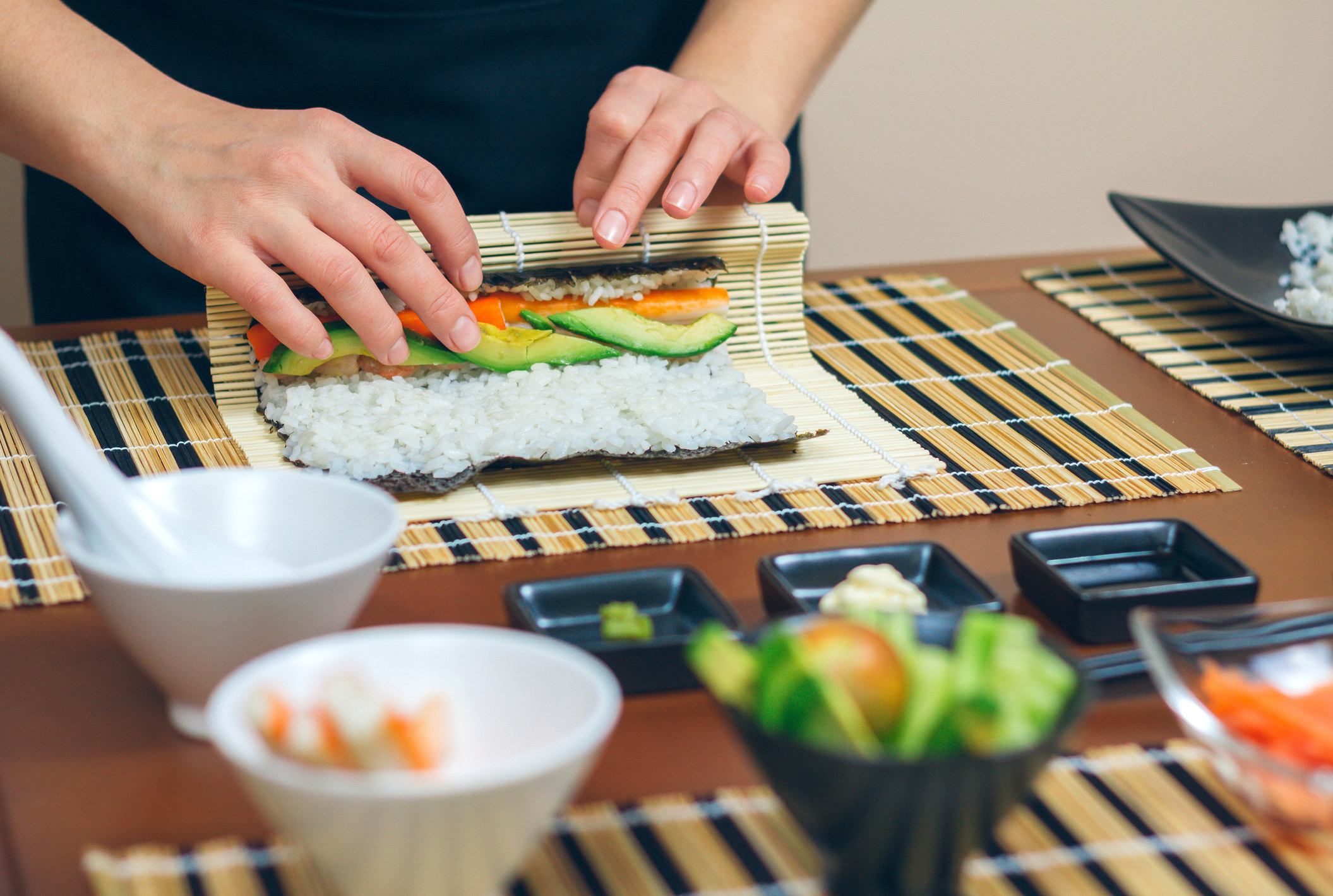 Detail of hands of person rolling up sushi.