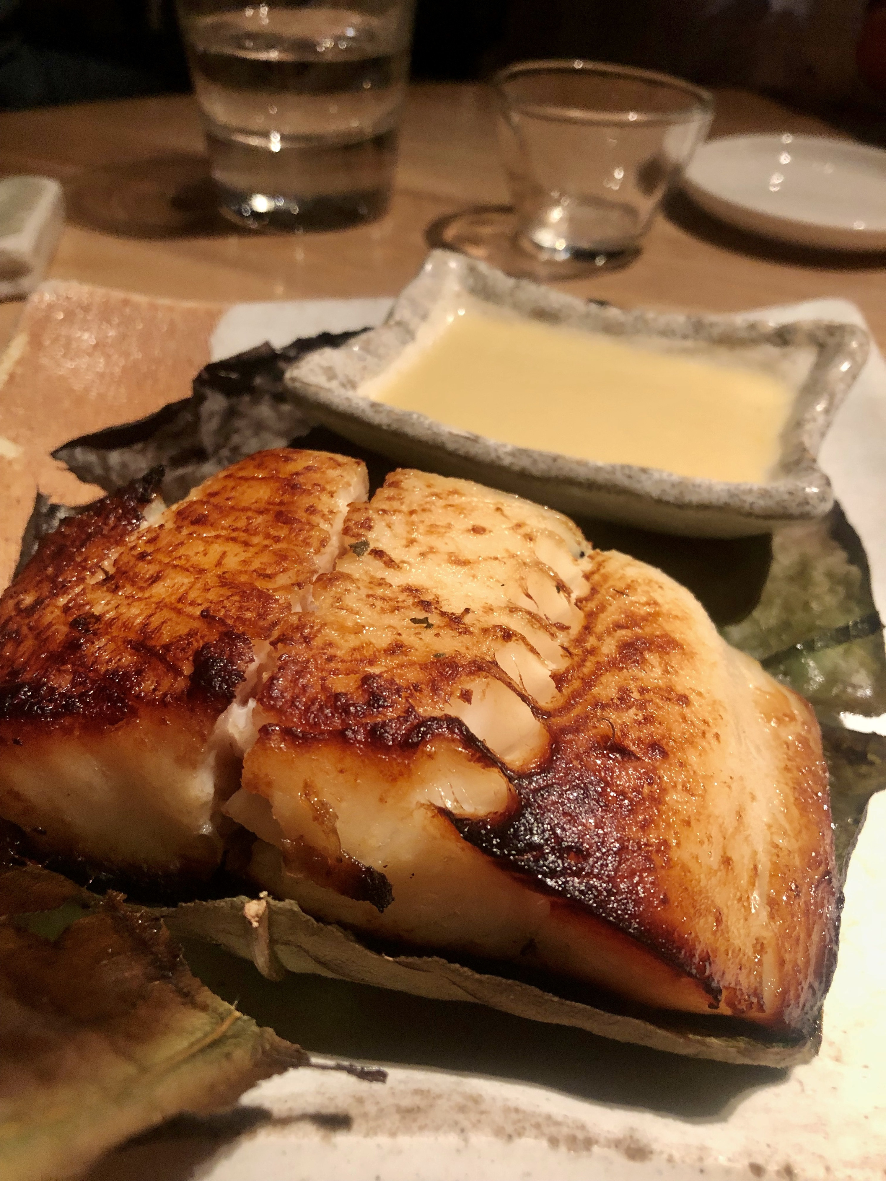 cod with a dark brown miso glaze on a plate with a dipping sauce