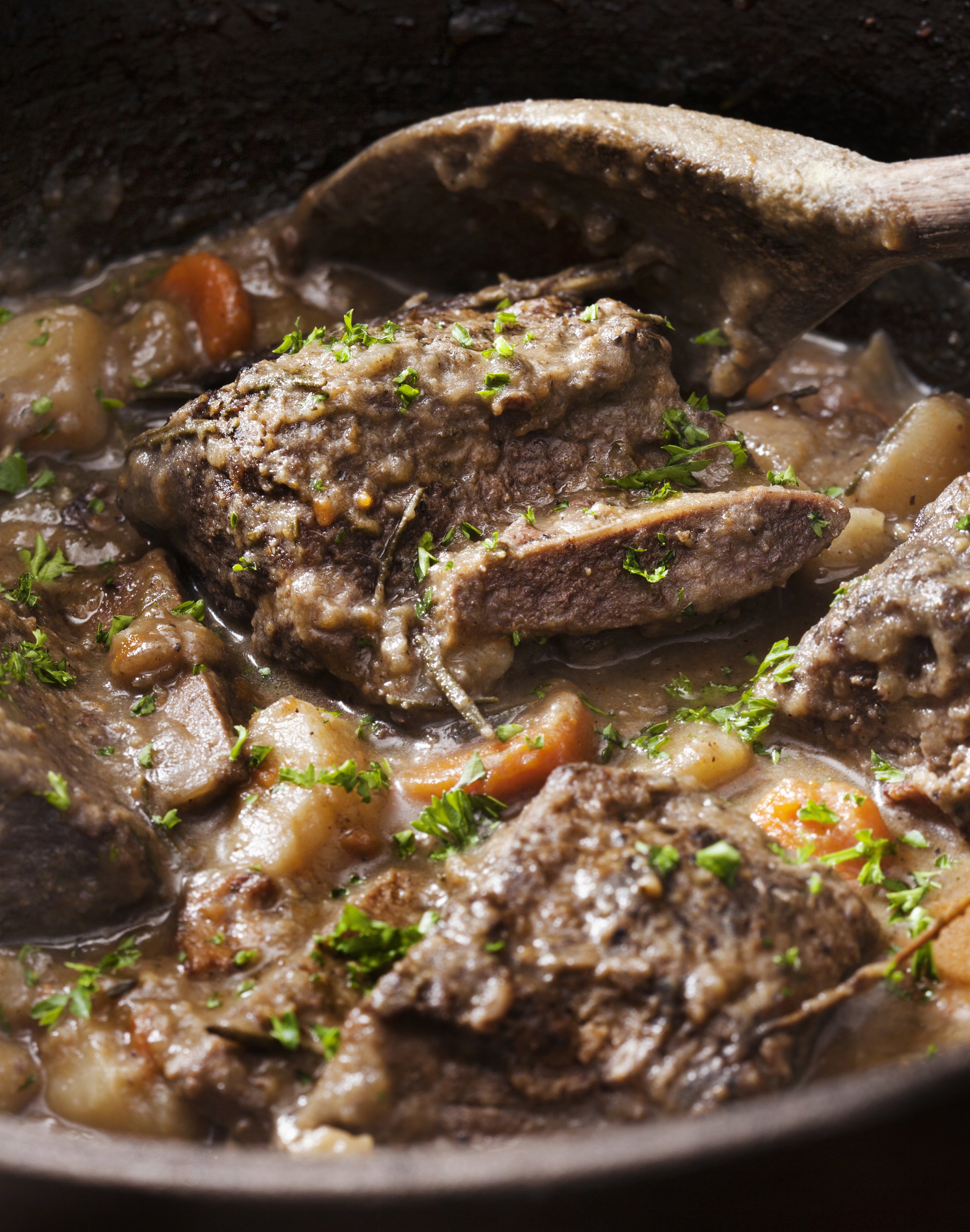 short ribs cooking in a gravy with vegetables, parsley sprinkled on top