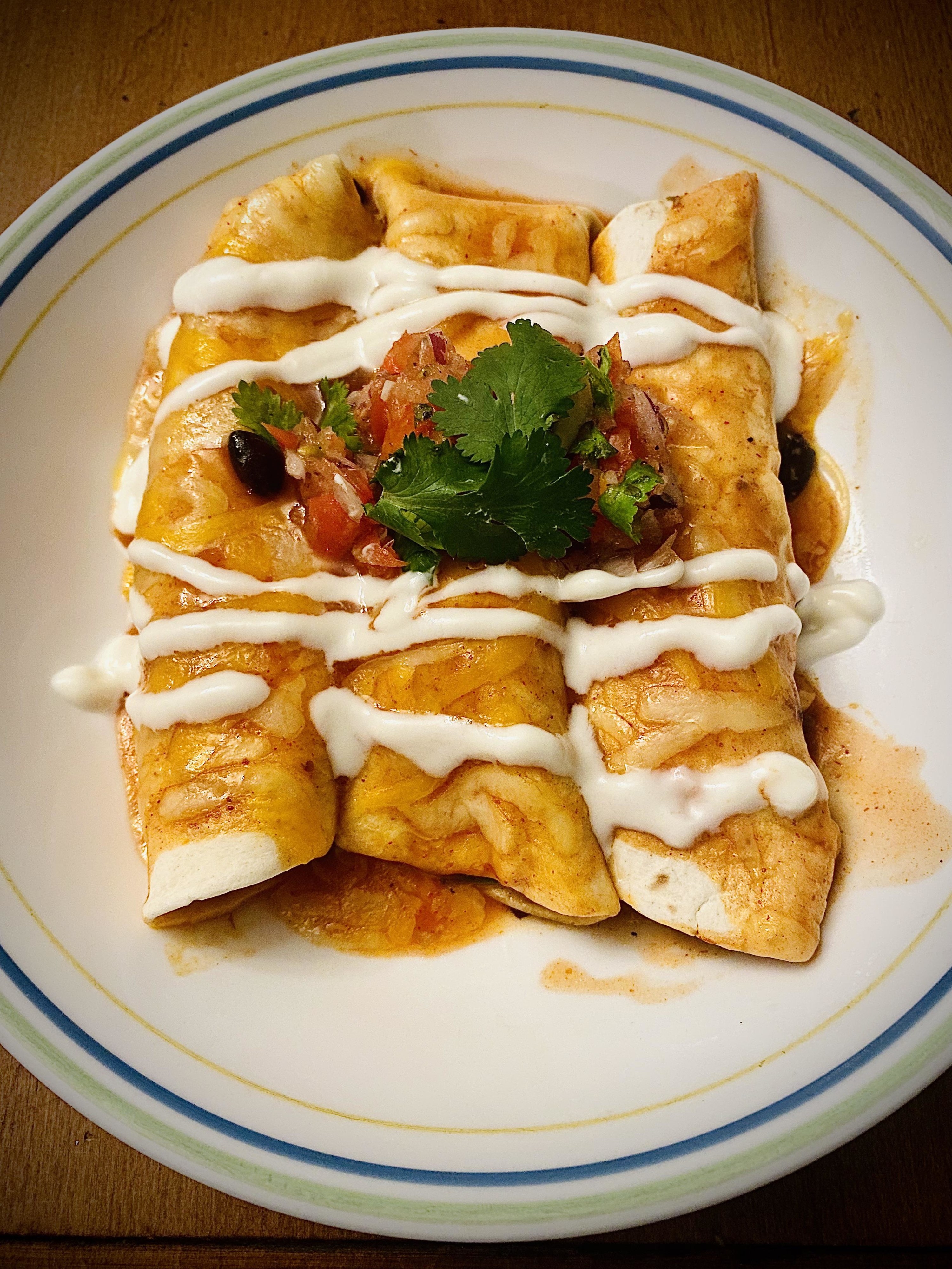 plate of three enchiladas, drizzled with crema and topped with enchilada sauce, cilantro, and salsa