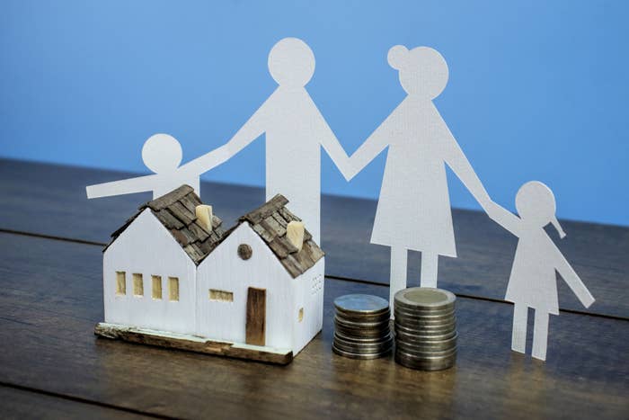 A paper cutout of a family next to a miniature model house and stack of coins