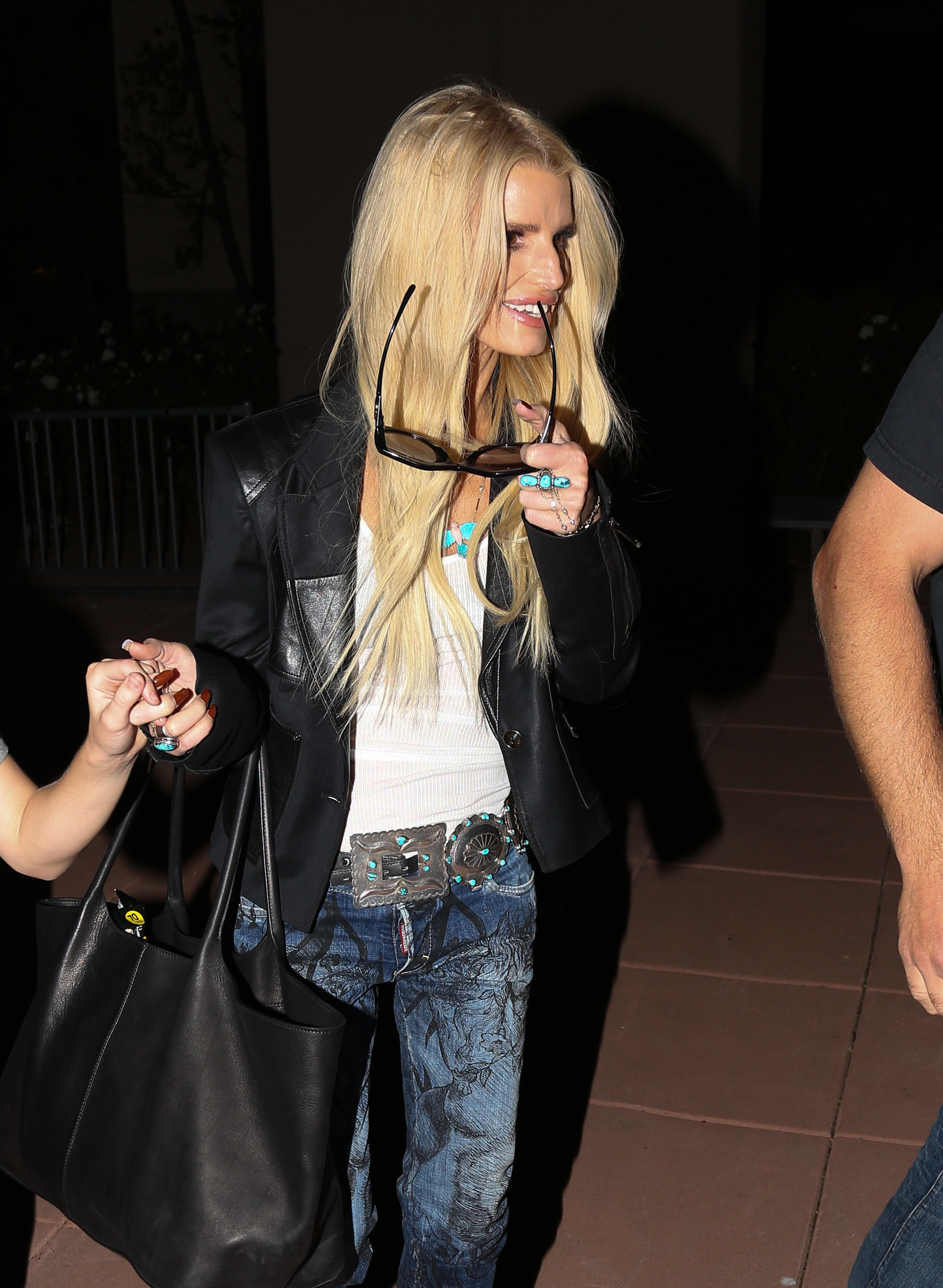 Jessica Simpson chews her sunglasses while walking at holding the hand of someone out of frame