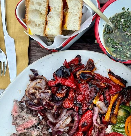 platters of fresh focaccia, seared steak and peppers, and chimichurri sauce on a dinner table outside