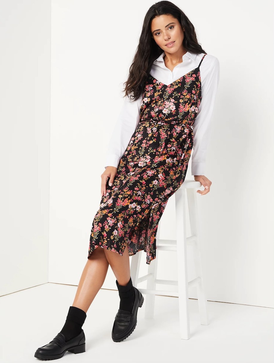 Model wearing black, white, yellow, and pink floral slip dress over white button down top with black shoes and socks
