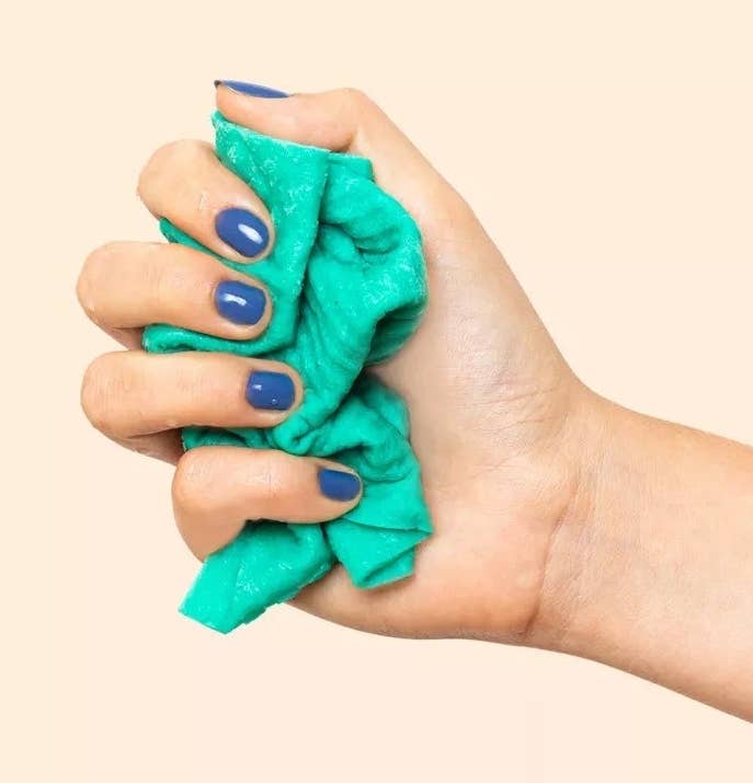 A model&#x27;s hand wringing out the electric blue dish cloth