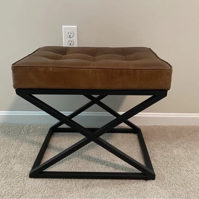 a reviewer photo of the leather ottoman with a brown tufted top and black base
