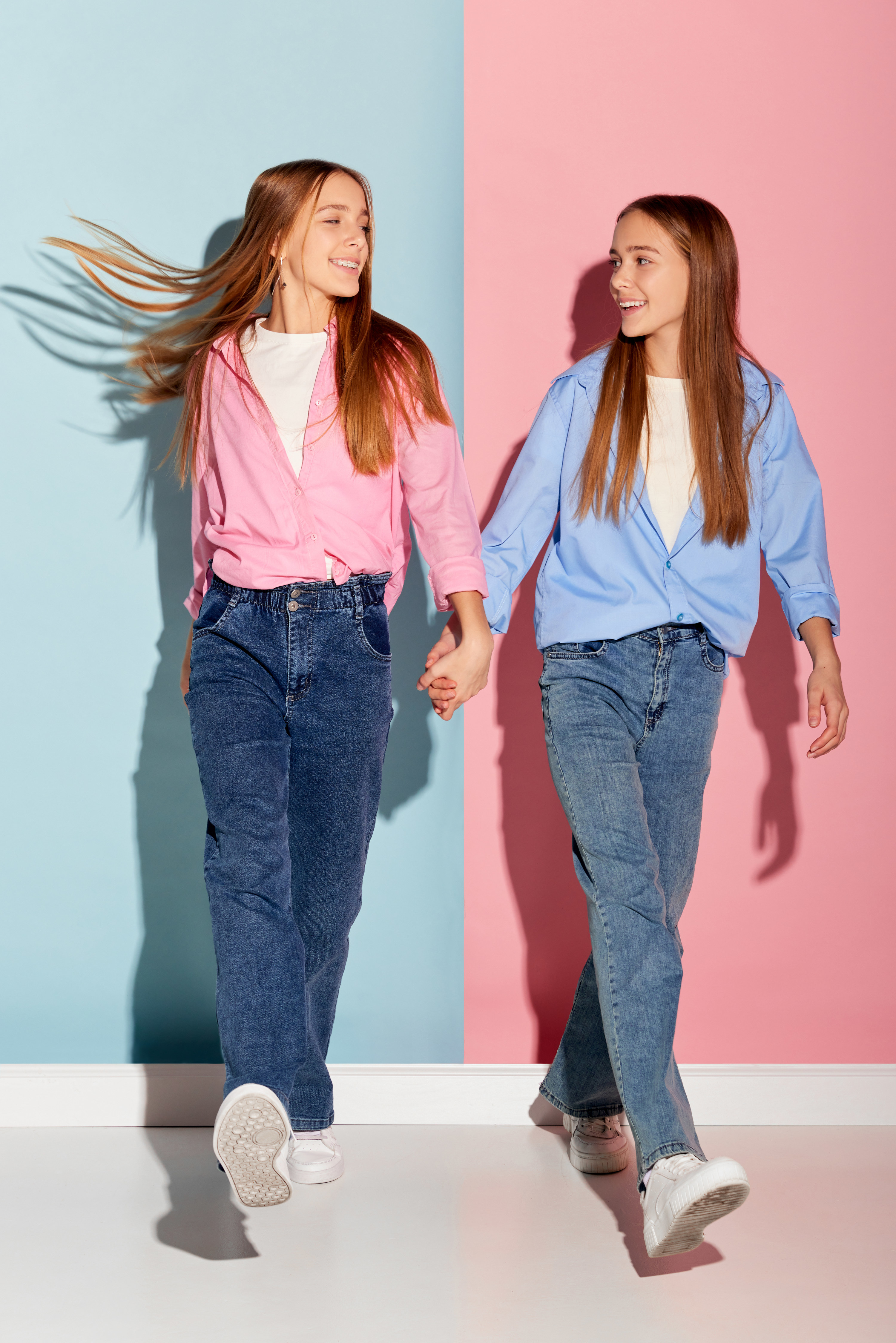Stylish couple of teen girls in trendy warm clothes walking over colorful background.