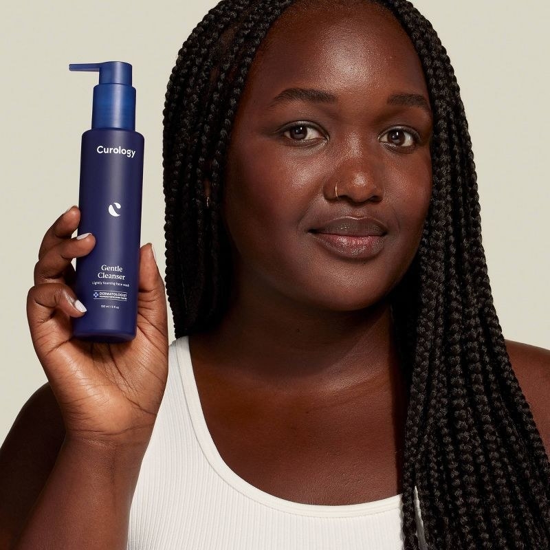 A person with braids holding a bottle of face cleanser