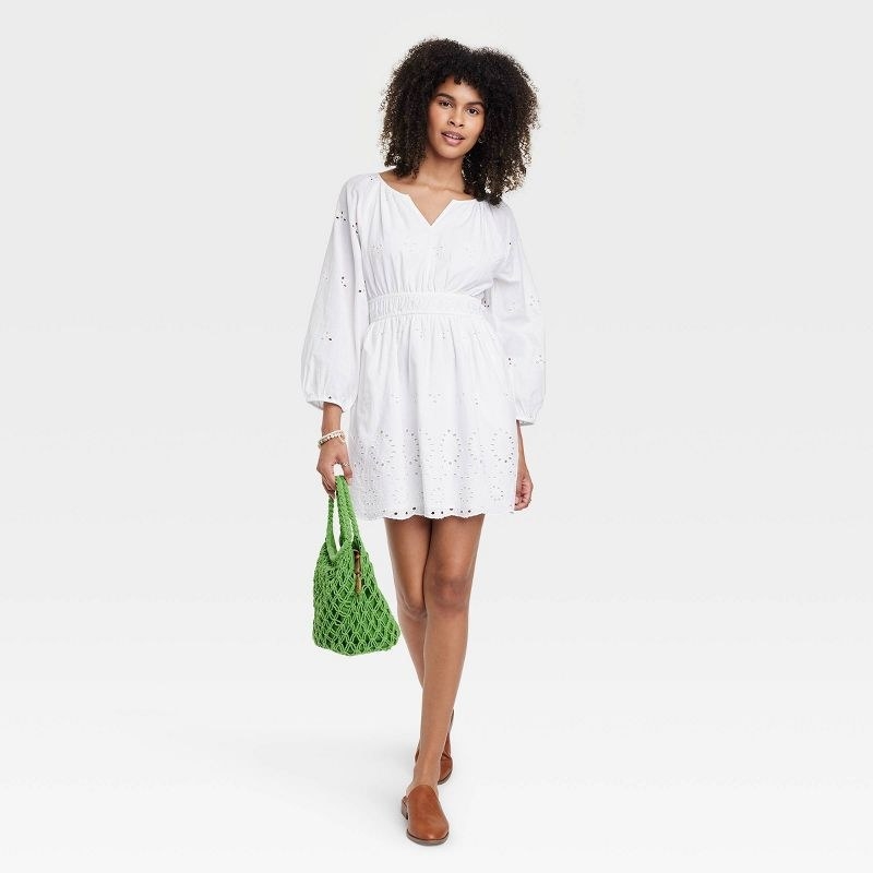 A model wearing the dress in white with a green handbag