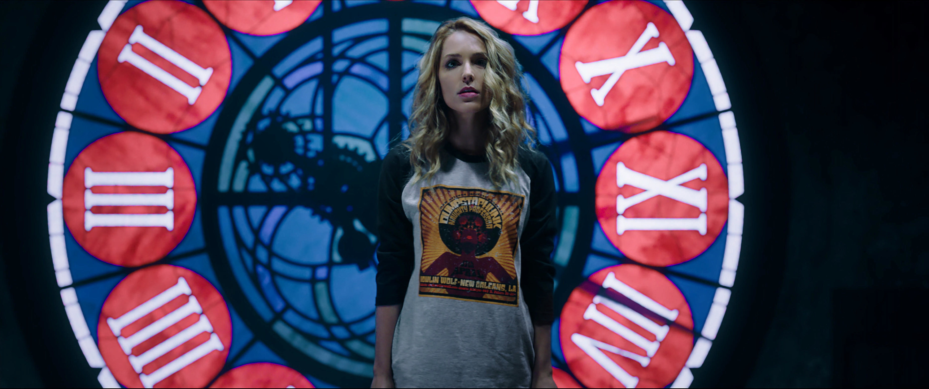 Jessica Rothe stands near a colorful and massive clock in the dark