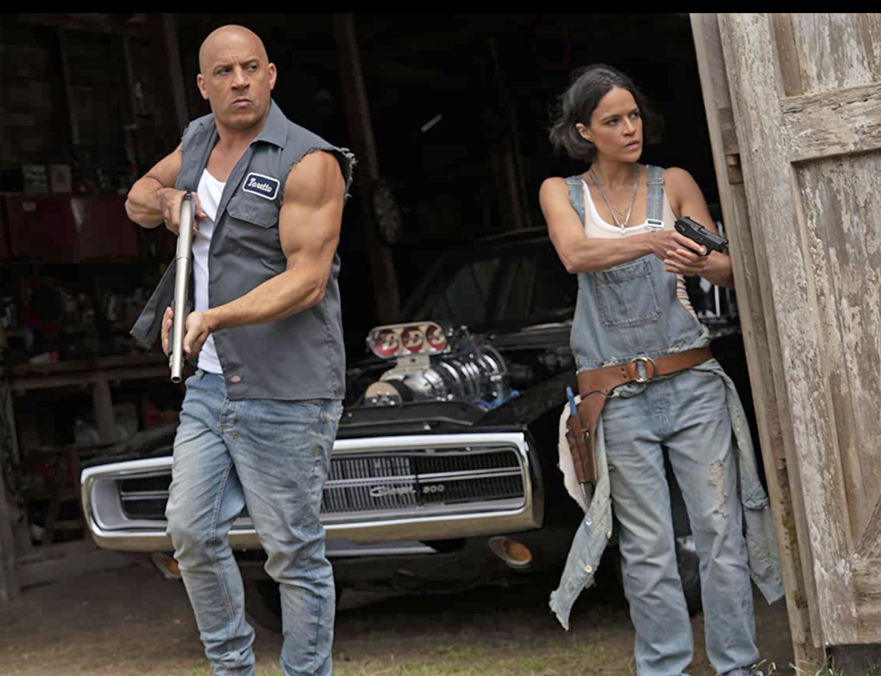 Vin Diesel and Michelle Rodriguez brandish guns while walking out of a dirty garage